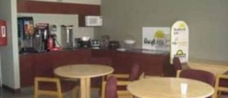 A small, simple cafe with round tables and chairs, a counter with a menu, and a microwave above it.