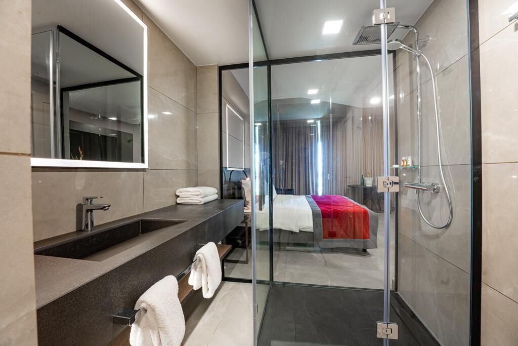 Un baño moderno con ducha envuelta en vidrio, un espejo grande y un lavamanos con toallero.