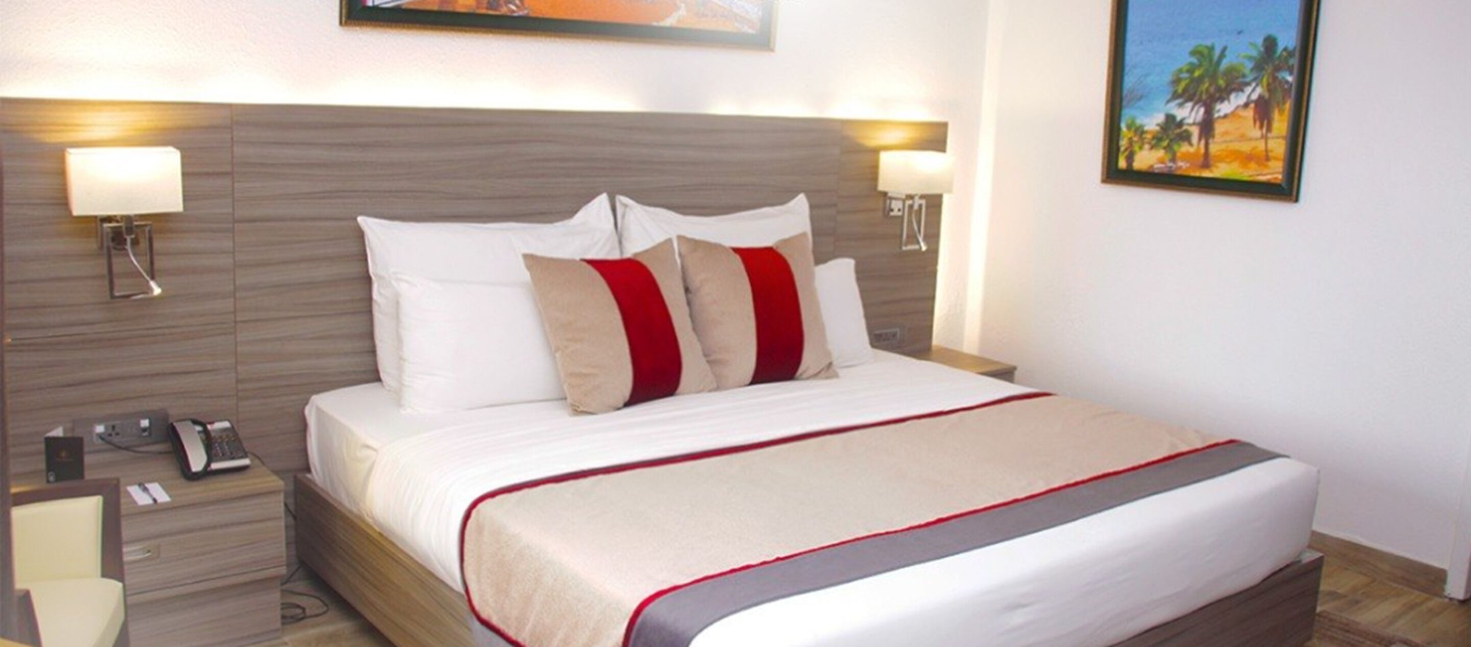 A hotel room with a large bed, two bedside lamps, a nightstand with a phone, and a painting on the wall.
