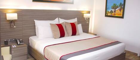 A hotel room with a large bed, two bedside lamps, a nightstand with a phone, and a painting on the wall.