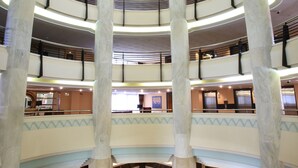 Un atrio de varios niveles con columnas de mármol, suelo a cuadros y una zona de estar central.