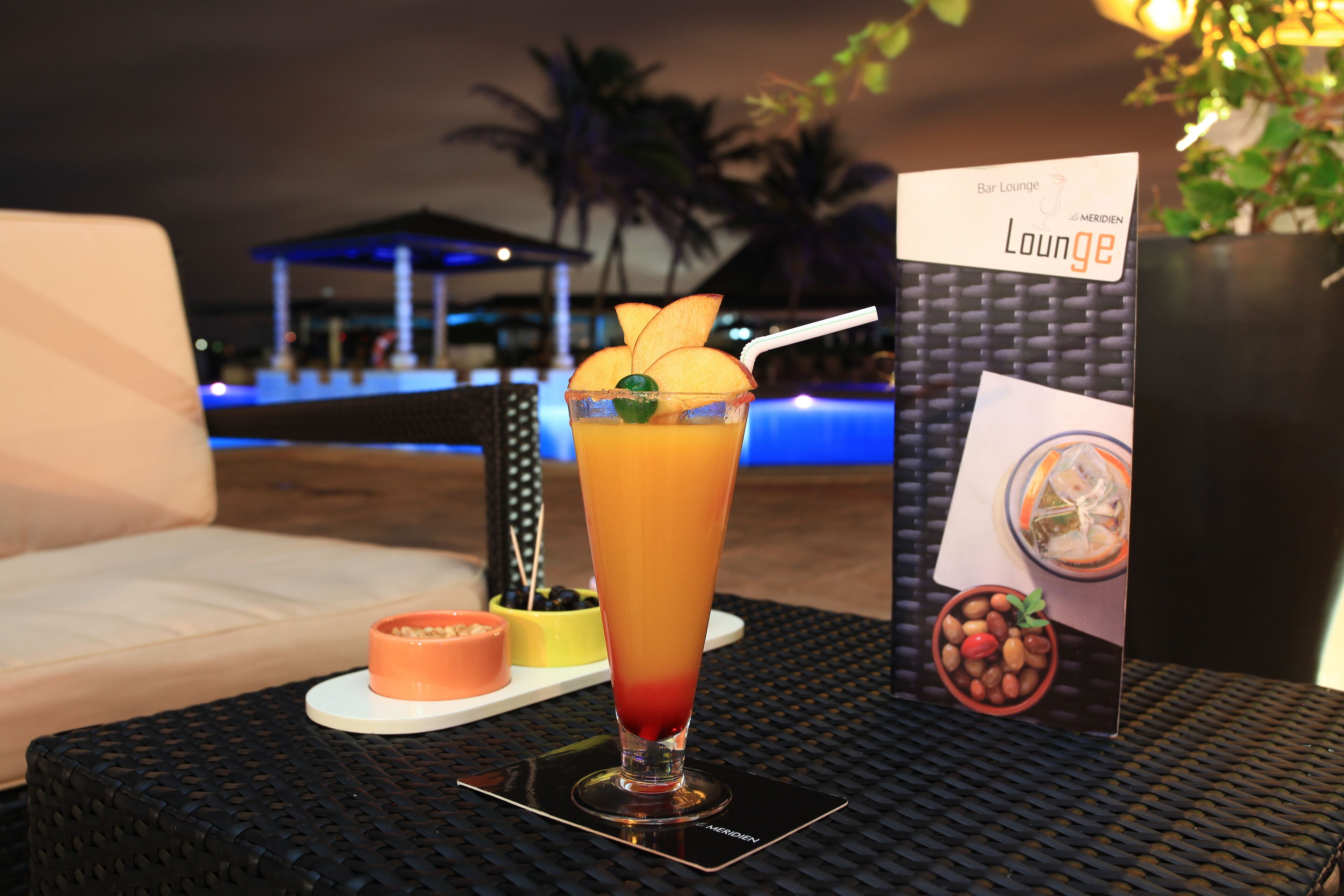 Un cocktail sur une table, accompagné d’un menu et d’un petit bol de noix.