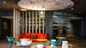 A modern lounge area with a circular ceiling design, a red sofa, and contemporary seating. - ibis Bordeaux Lac (Bordeaux)