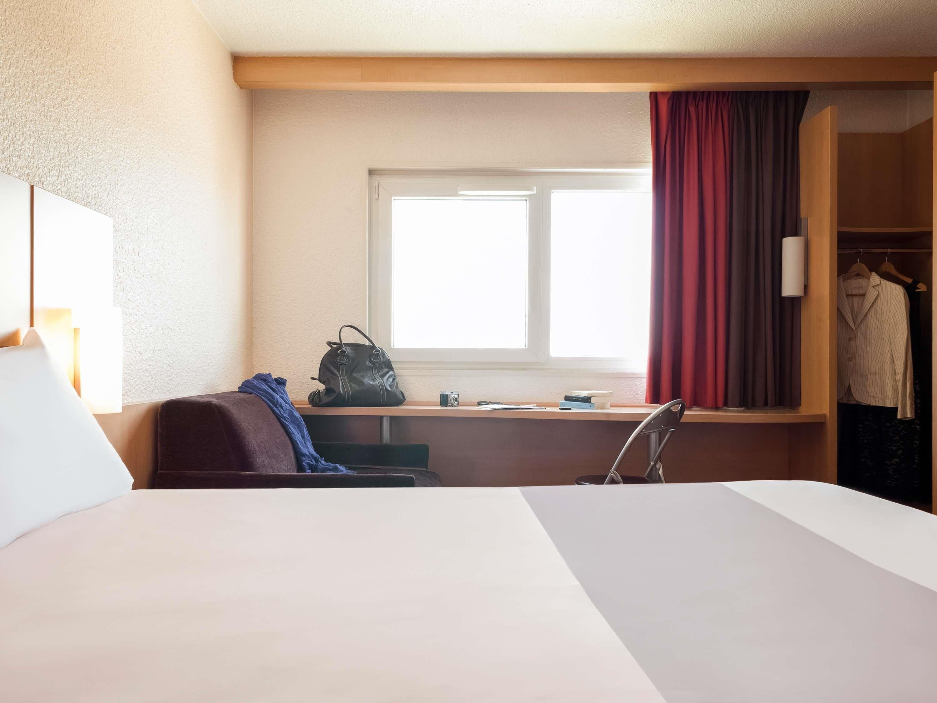 Een hotelkamer met een bed, een bureau met stoel, een raam met gordijnen en een kledingkast.