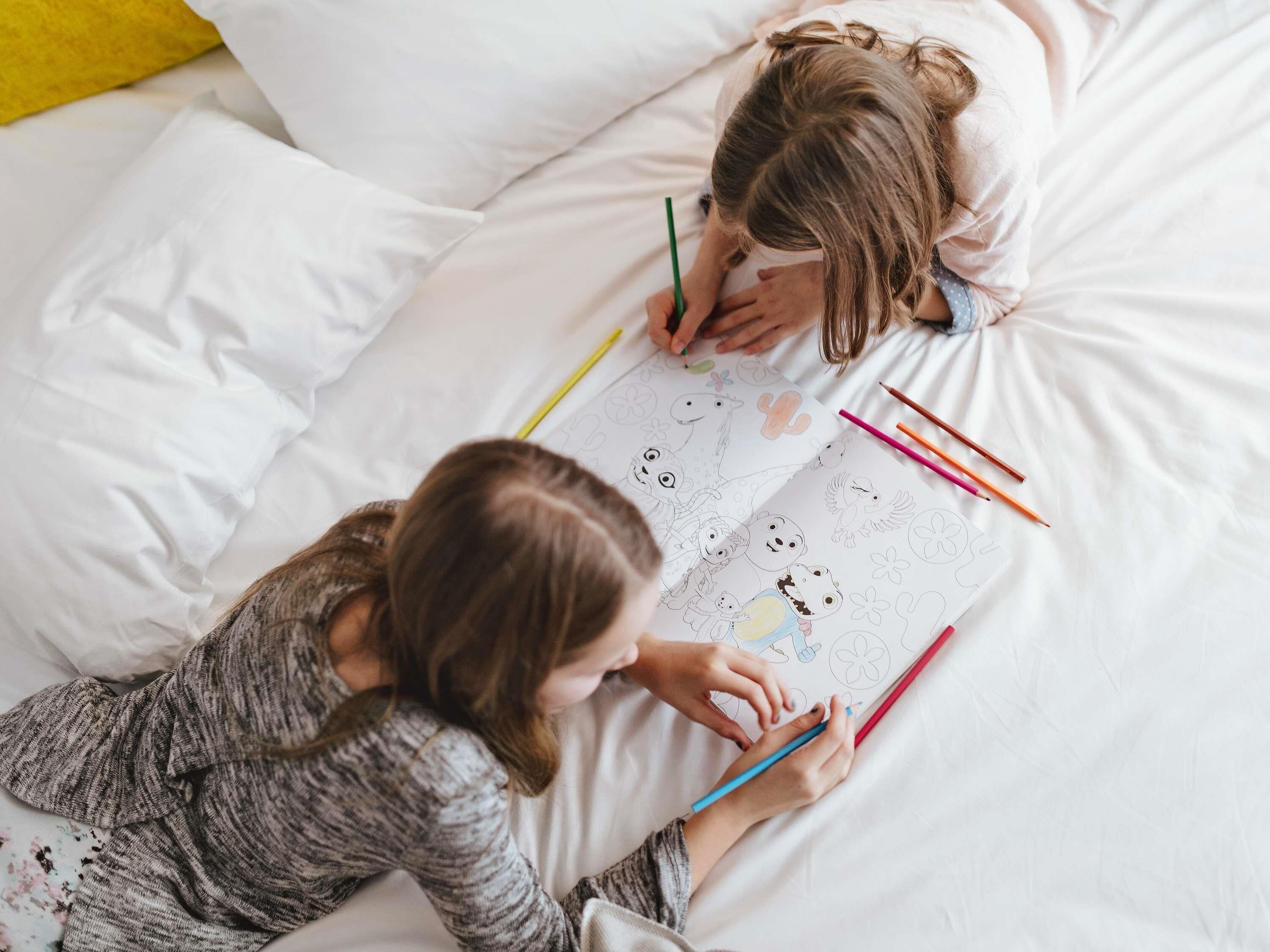 Dos personas descansando en una cama con un cuaderno de dibujos y lápices de colores.