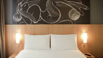Une chambre d’hôtel avec une grande œuvre d’art abstraite accrochée au mur, une tête de lit en bois, deux lampes de chevet et une télécommande posée sur la table de chevet.