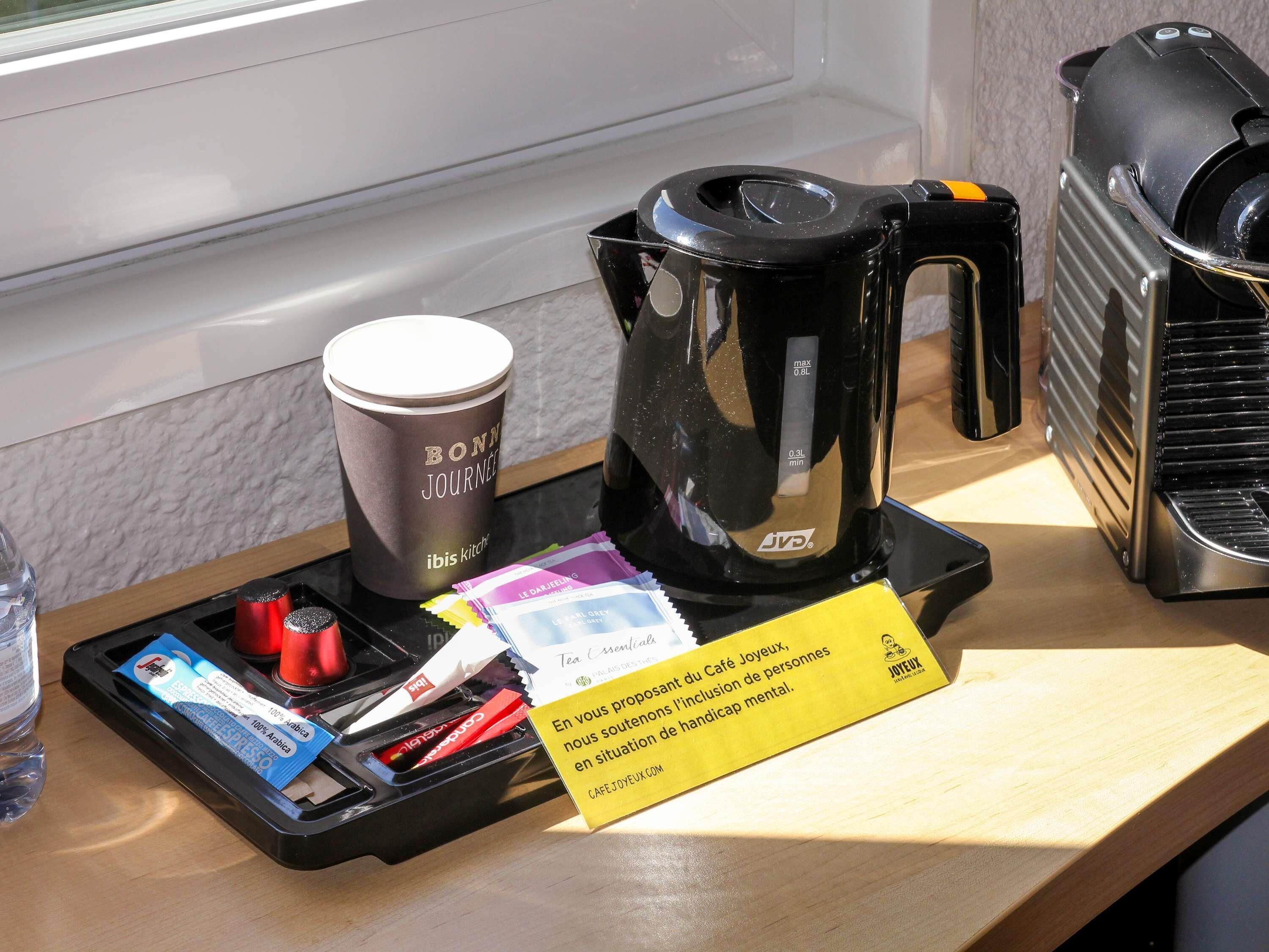 A coffee station with a coffee maker, a cup, and tea packets.