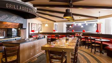 Interior de restaurante con barra, mesas de madera y cabinas rojas.