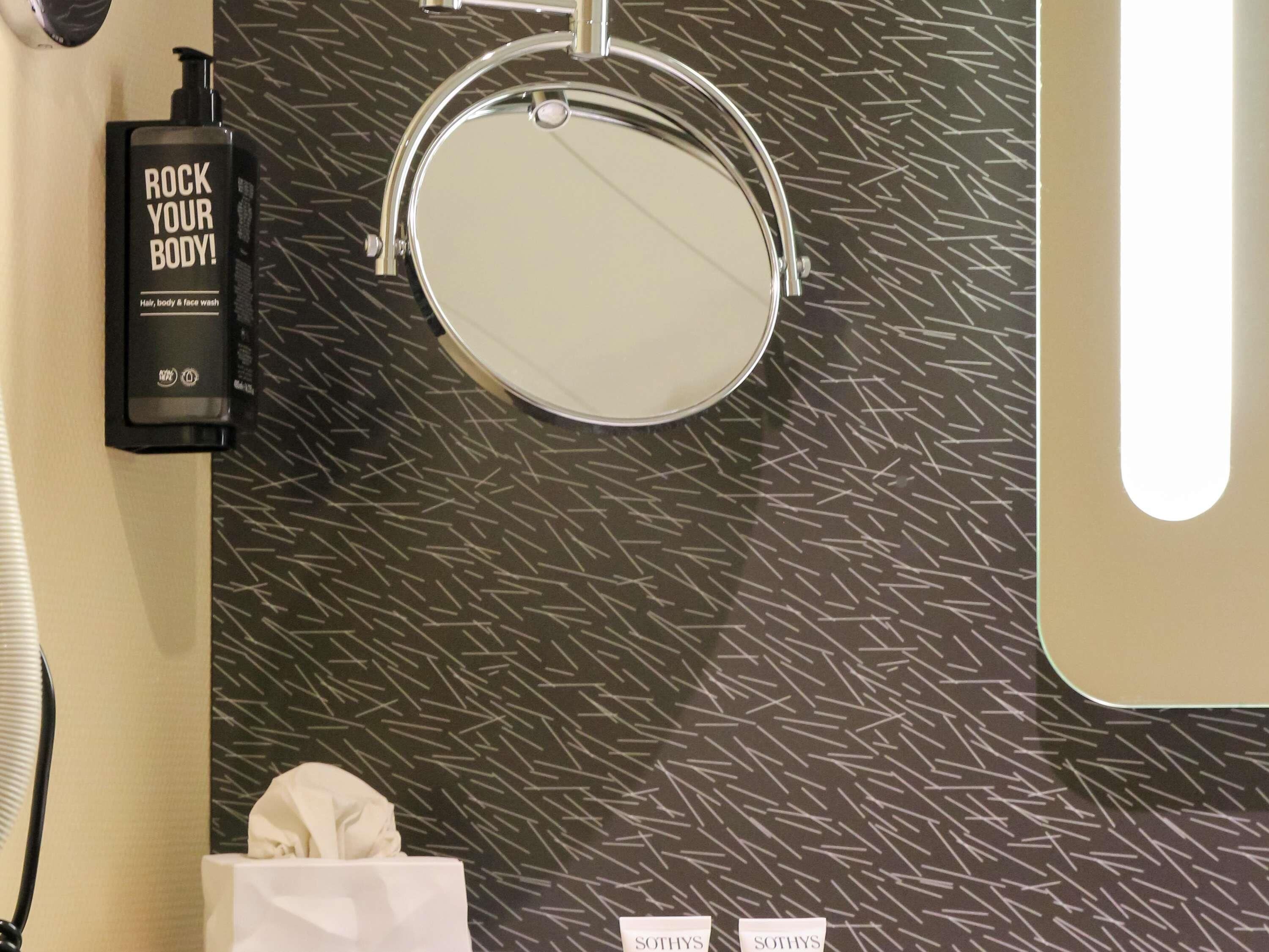 A bathroom with a mirror, a black bottle labeled 'ROCK YOUR BODY!', and a towel on a white surface.