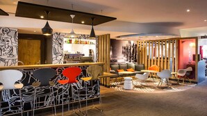A modern bar area with a bar counter, seating with chairs and tables, and a decorative wall with abstract designs. - ibis Bordeaux Lac (Bordeaux)