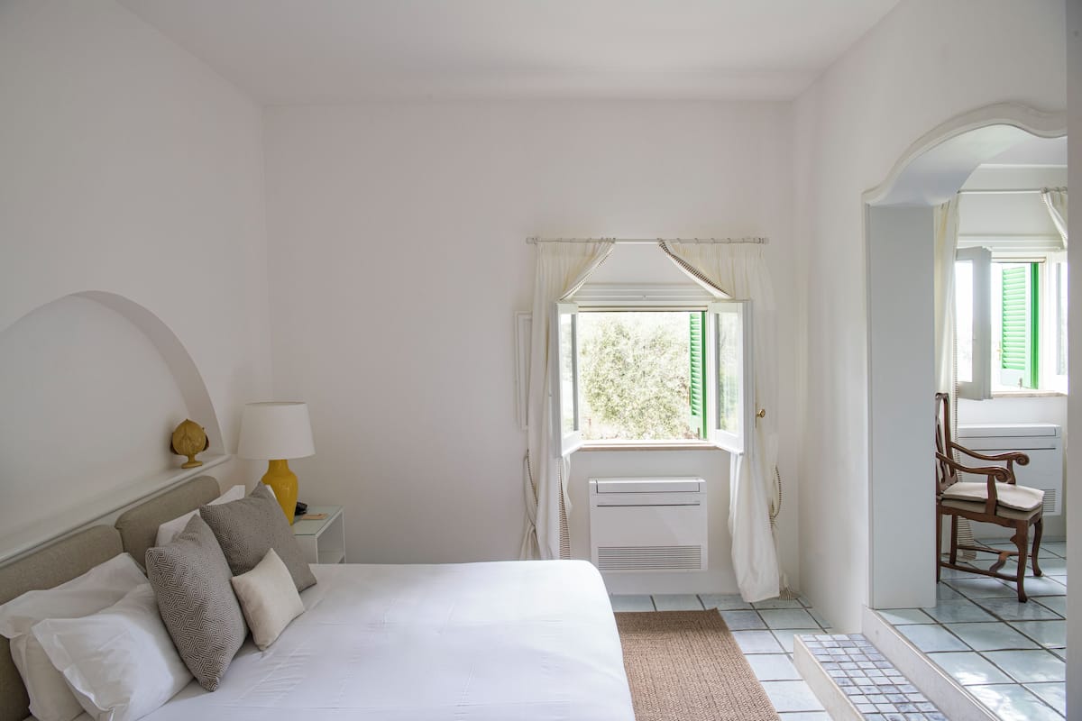 Une chambre à coucher avec un lit, une table de chevet avec une lampe, une chaise et une fenêtre avec des rideaux.