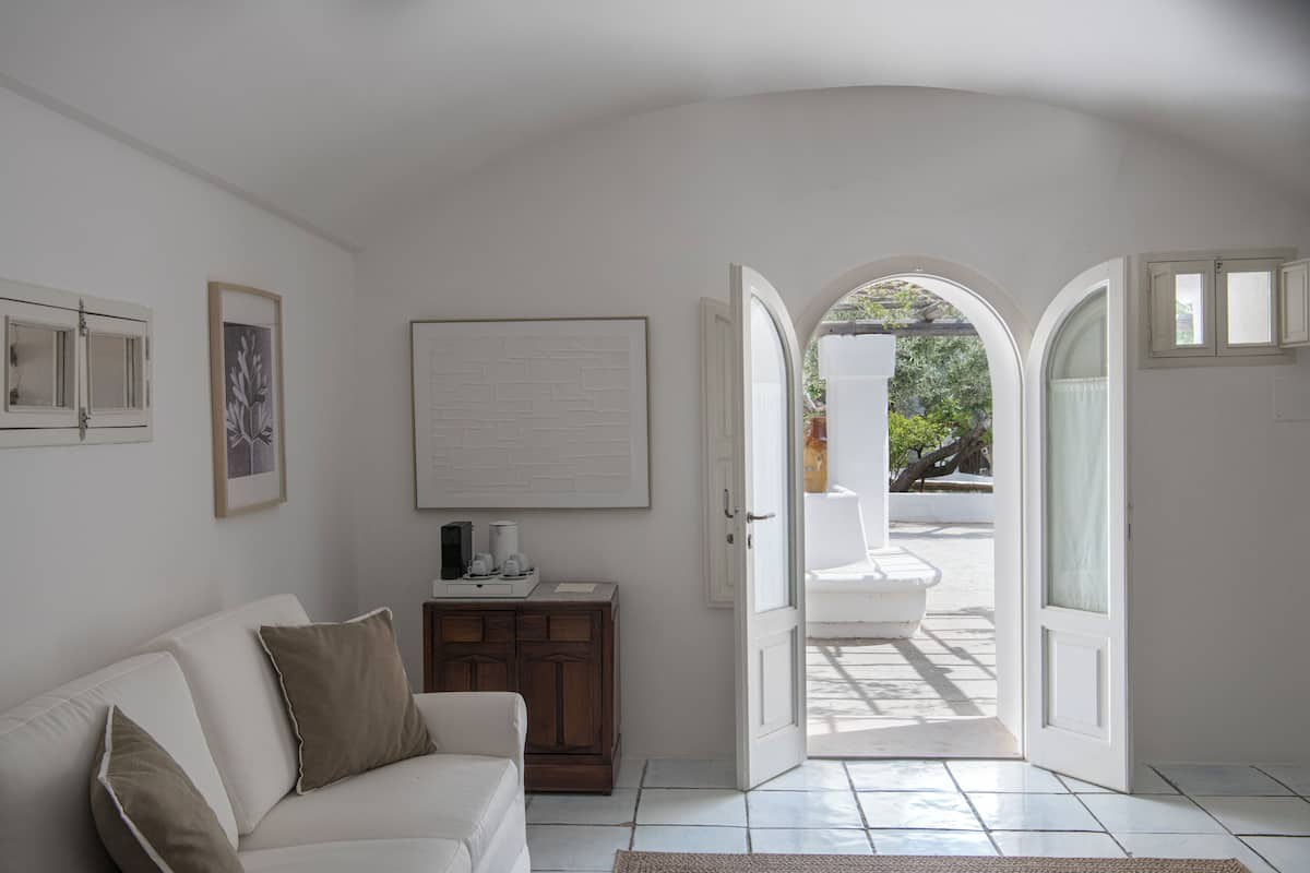 Une pièce avec un canapé blanc, un meuble en bois et une porte donnant sur un espace extérieur où se trouvent une chaise blanche et une table.