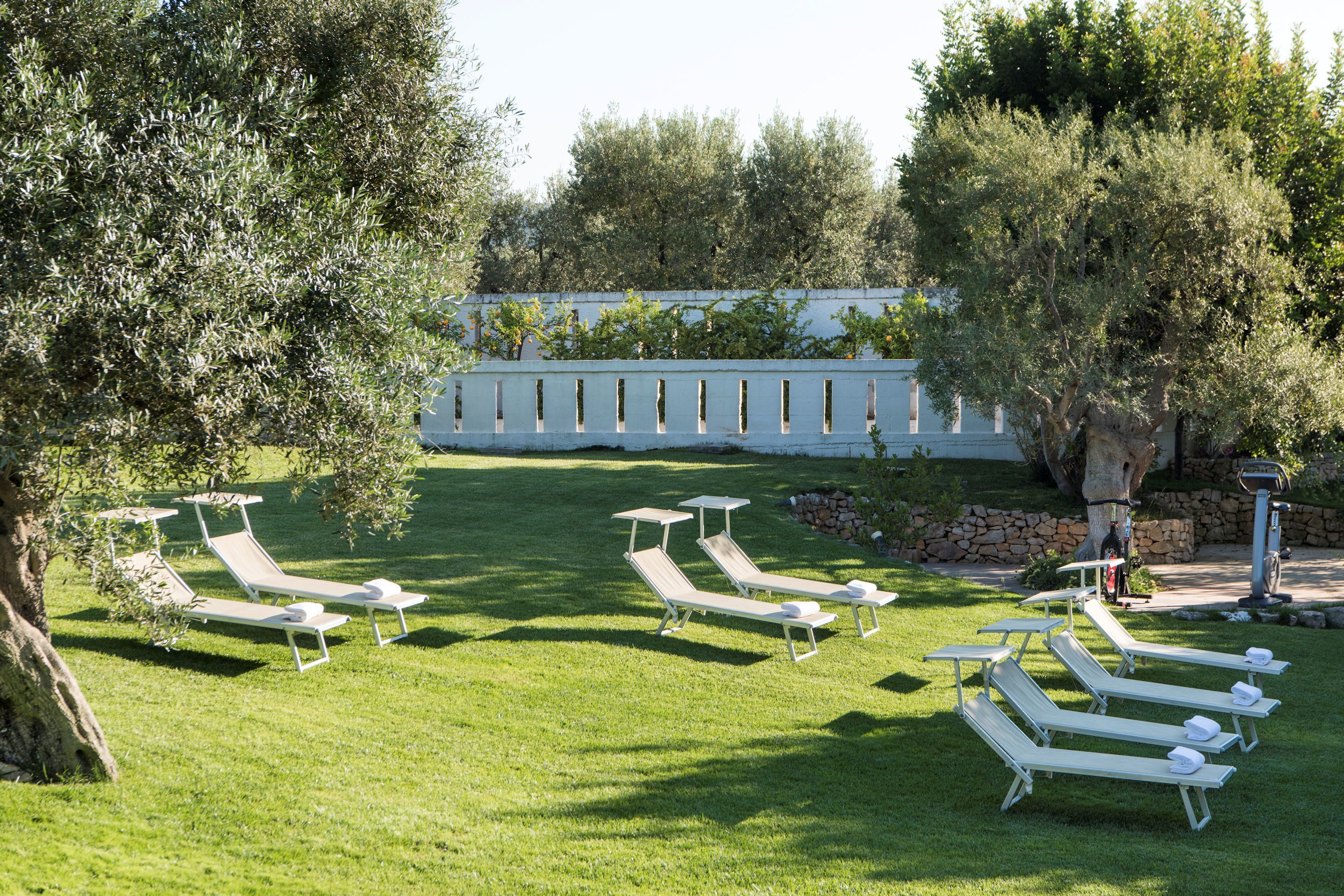 A well-maintained outdoor area with multiple sun loungers and tables, surrounded by lush greenery and trees.