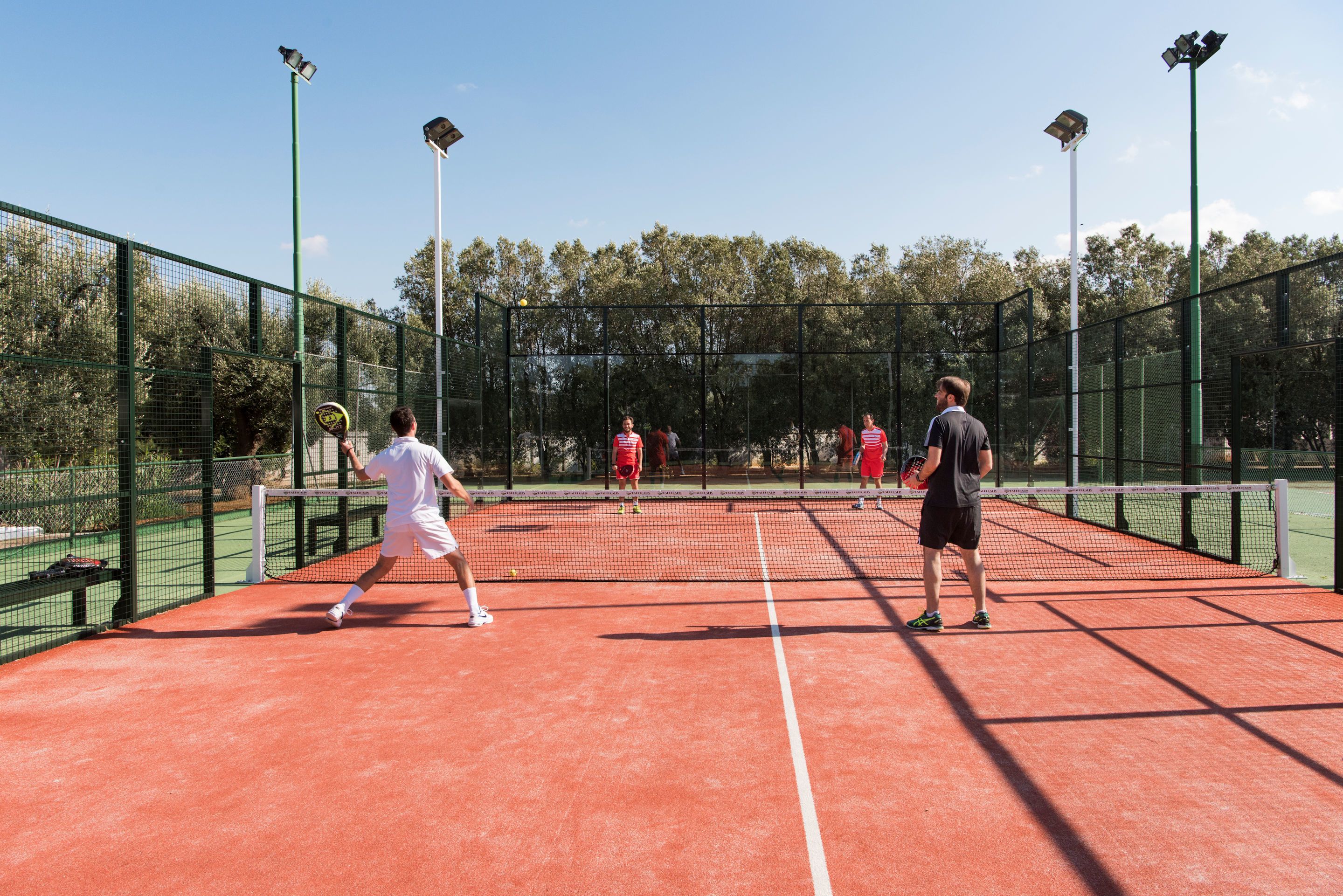 Un court de tennis avec des joueurs, un filet et une clôture qui l’entoure.