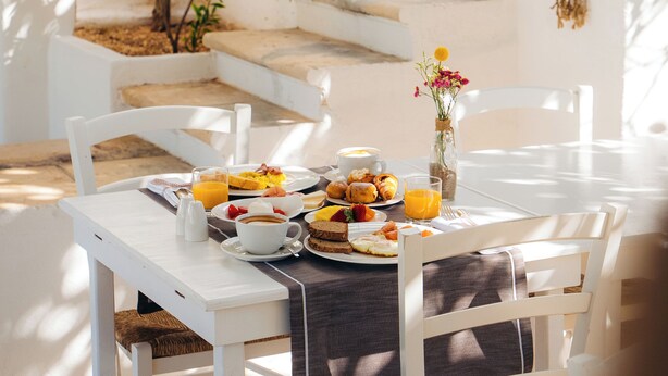 A breakfast table set with various dishes, a vase with flowers, and a staircase in the background. - Il Melograno (Monopoli)