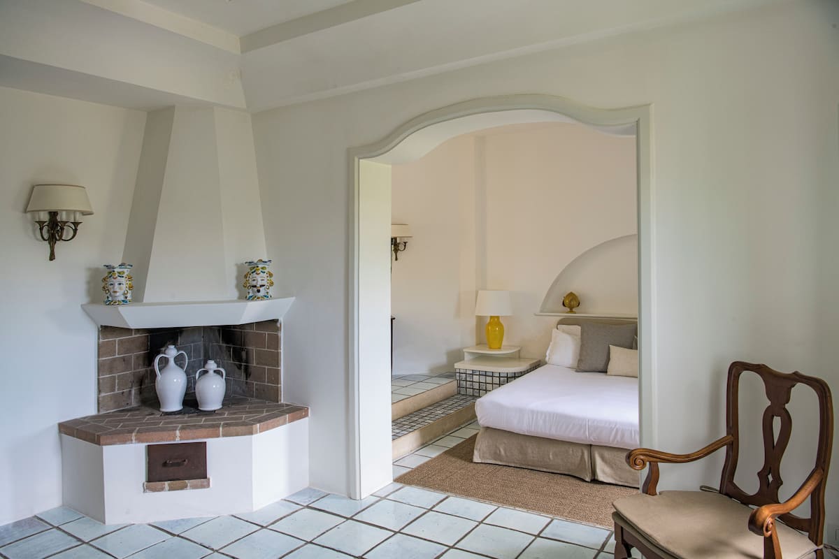 Une chambre à coucher avec une cheminée, un lit, une chaise et une table de chevet avec une lampe.