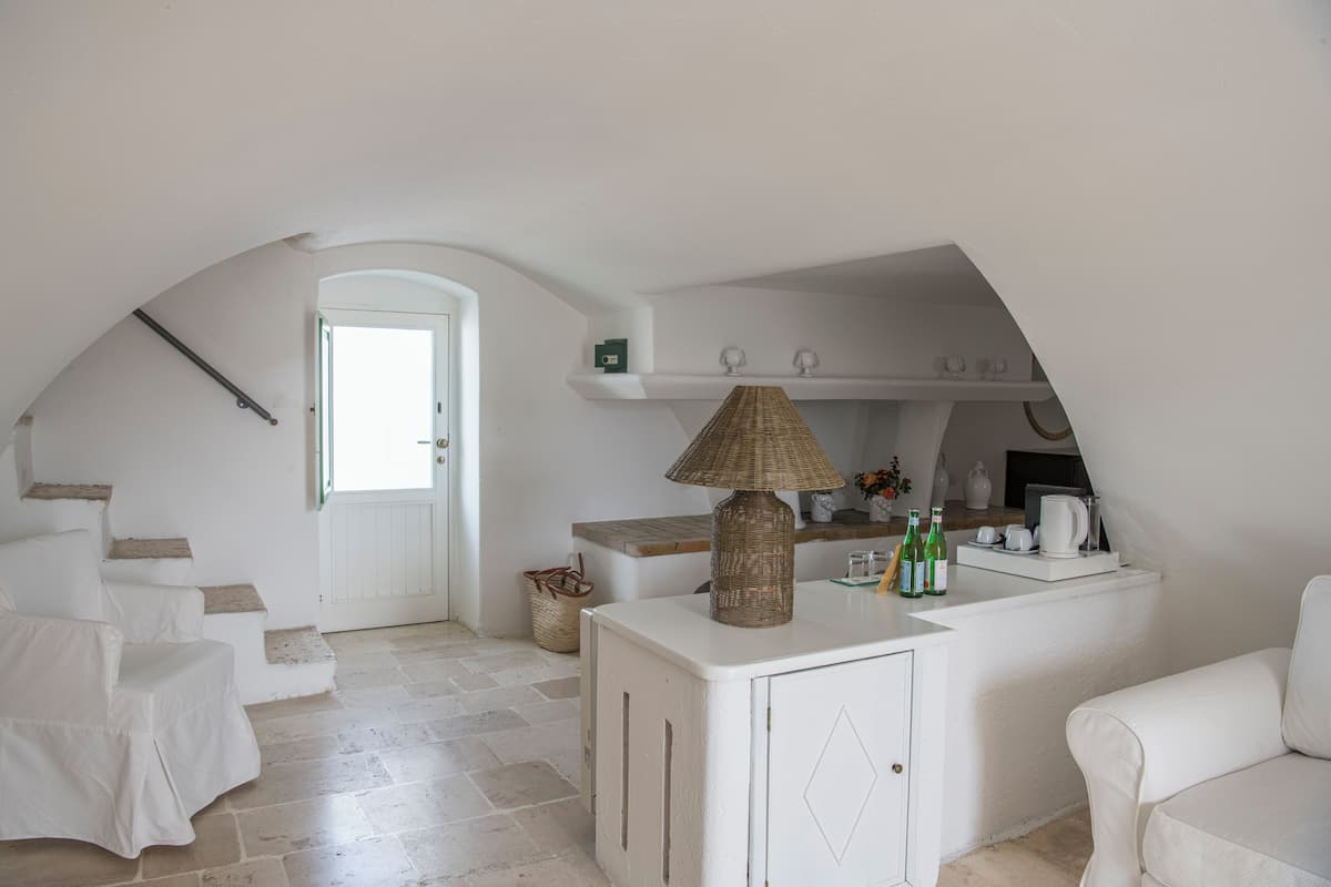 Un intérieur blanc avec un coin cuisine, une lampe en osier et un canapé blanc.
