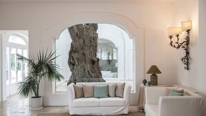 A spacious room with a large tree trunk centerpiece, a white sofa, and a matching armchair. - Il Melograno (Monopoli)