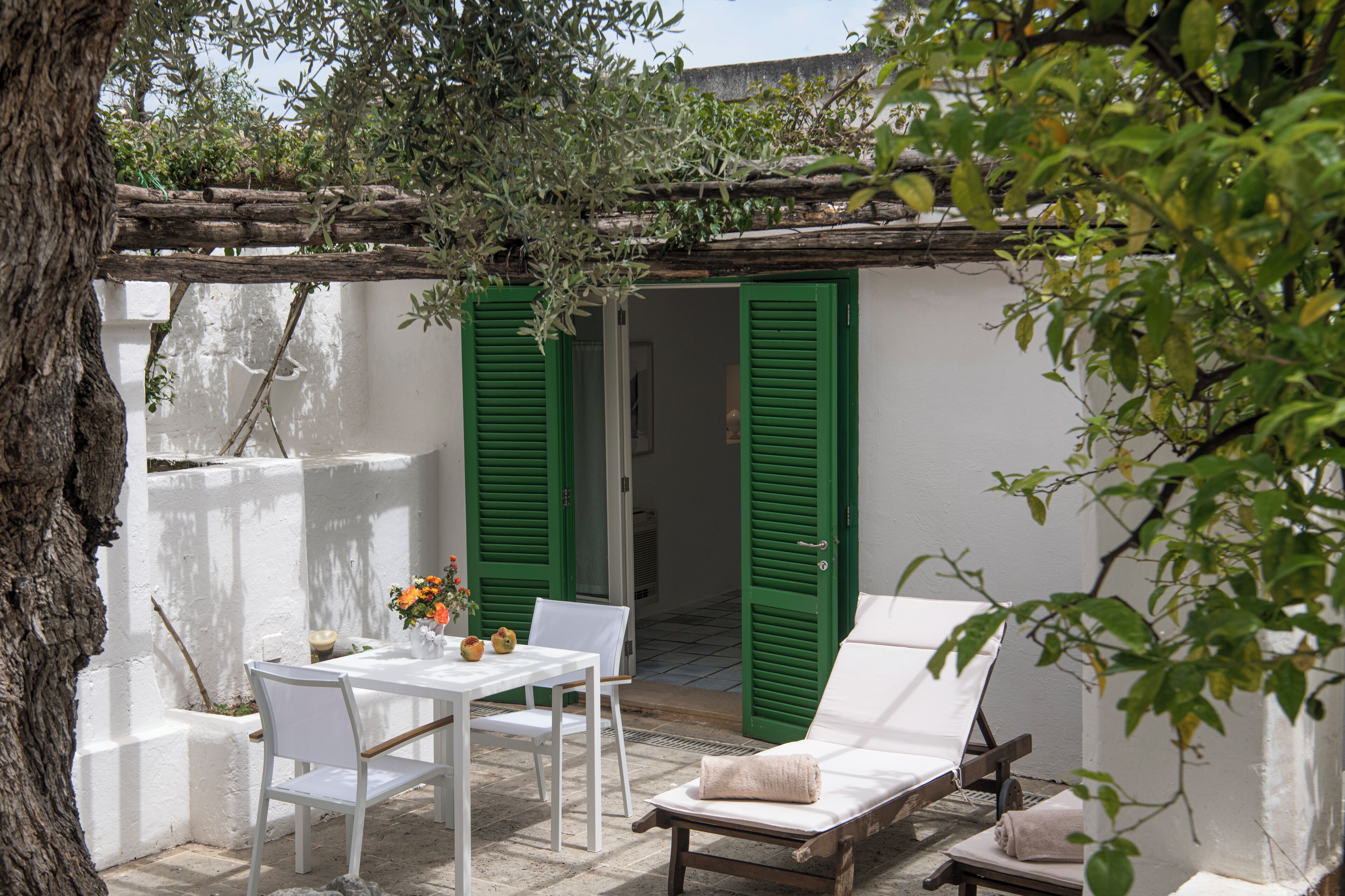 Une terrasse avec une table et des chaises, un fauteuil de relaxation et des volets verts.