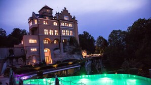 Un edificio grande, de estilo castillo, con muchas ventanas y una piscina al frente.