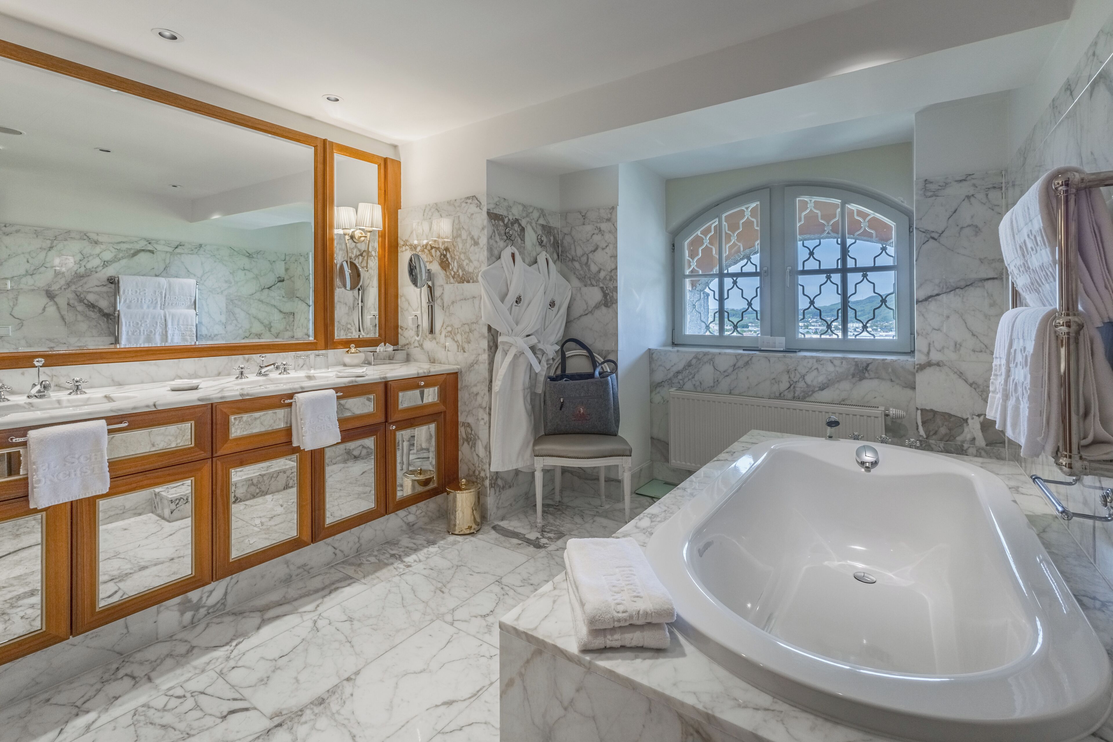 A bathroom with a marble floor, a large bathtub, a vanity with a mirror, and a window with a decorative grille.