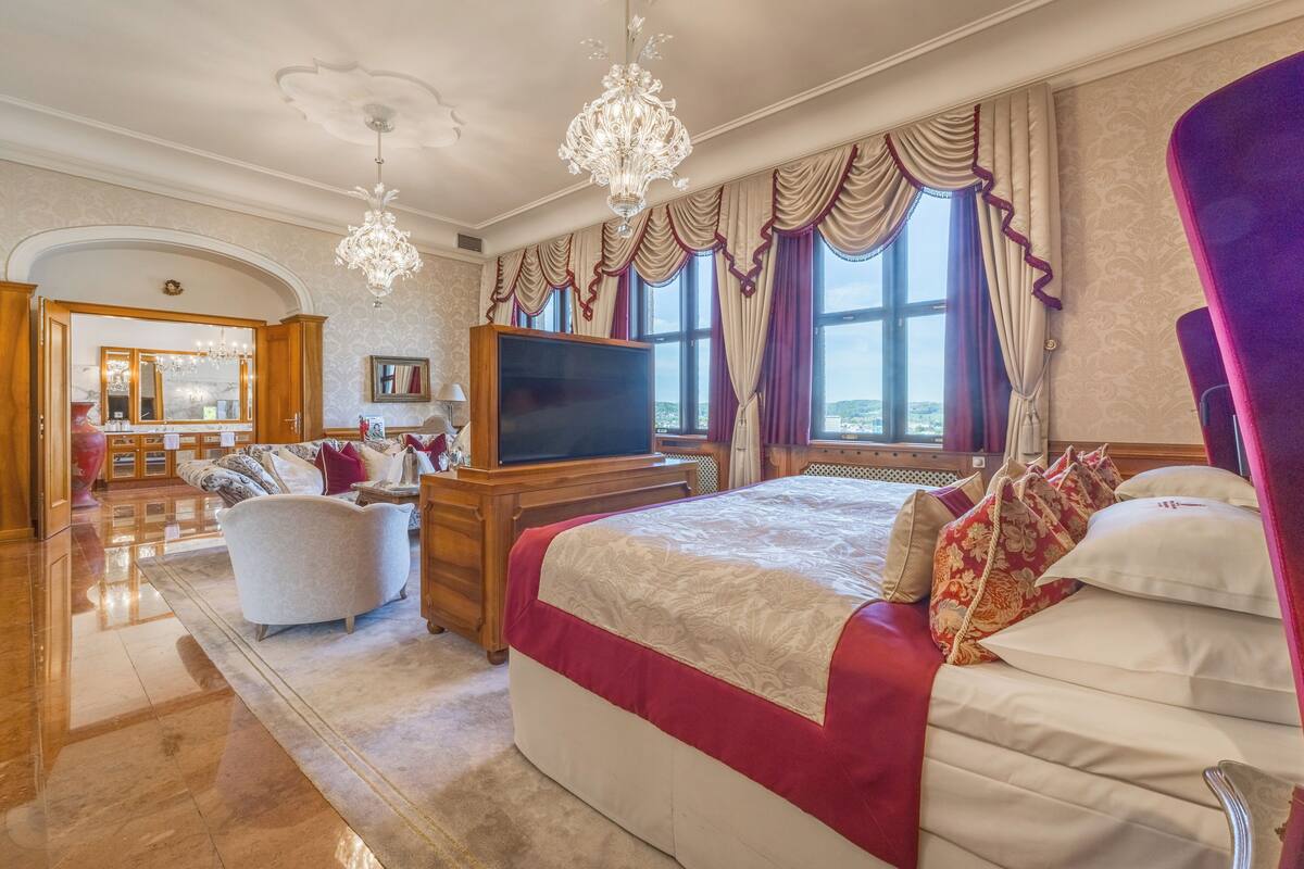 A spacious bedroom with a large bed, a television, and a view of the city.