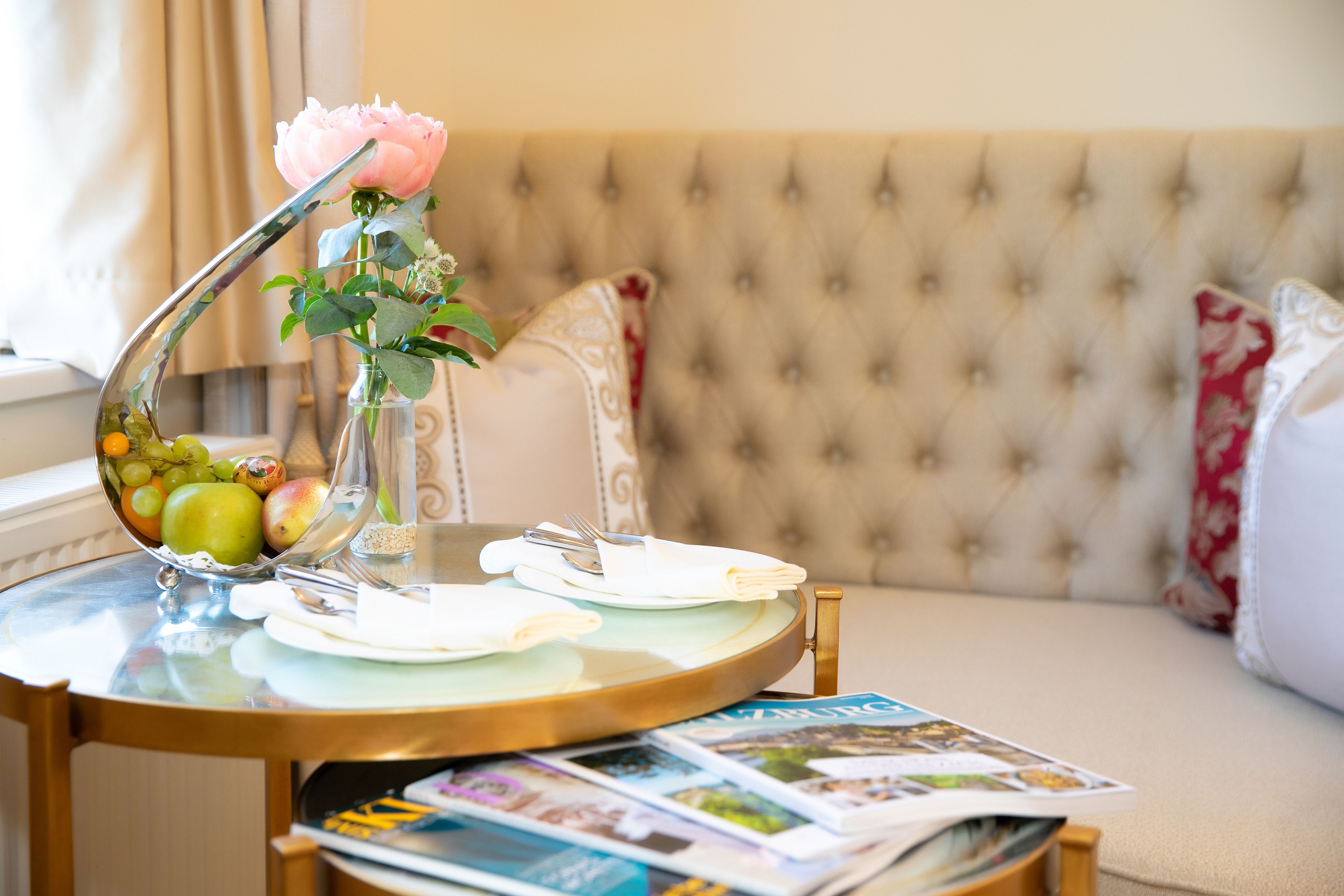 A dining table with a vase of flowers, plates, cutlery, and magazines.