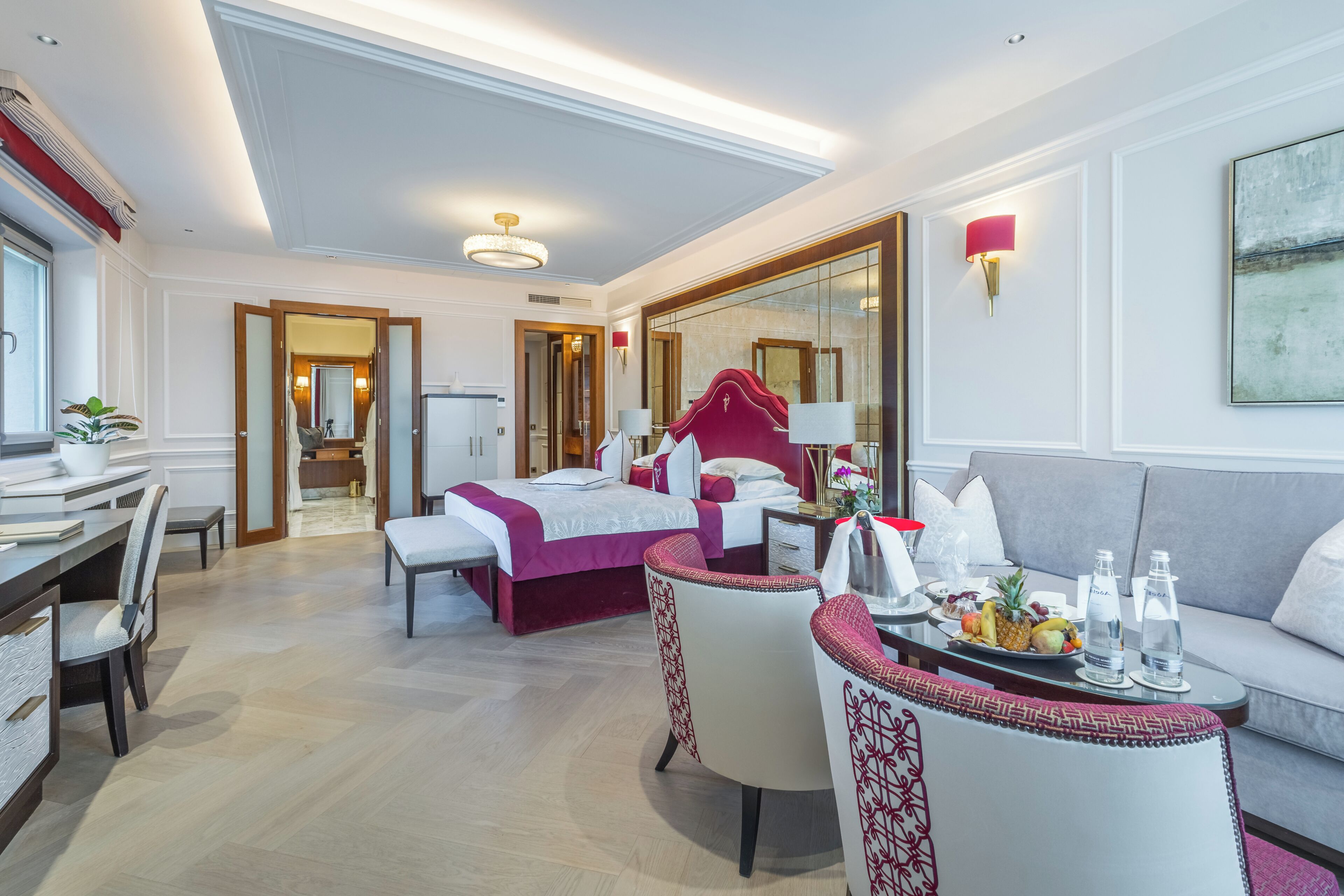 A hotel room with a bed, a sofa, a dining table with chairs, and a mirror.