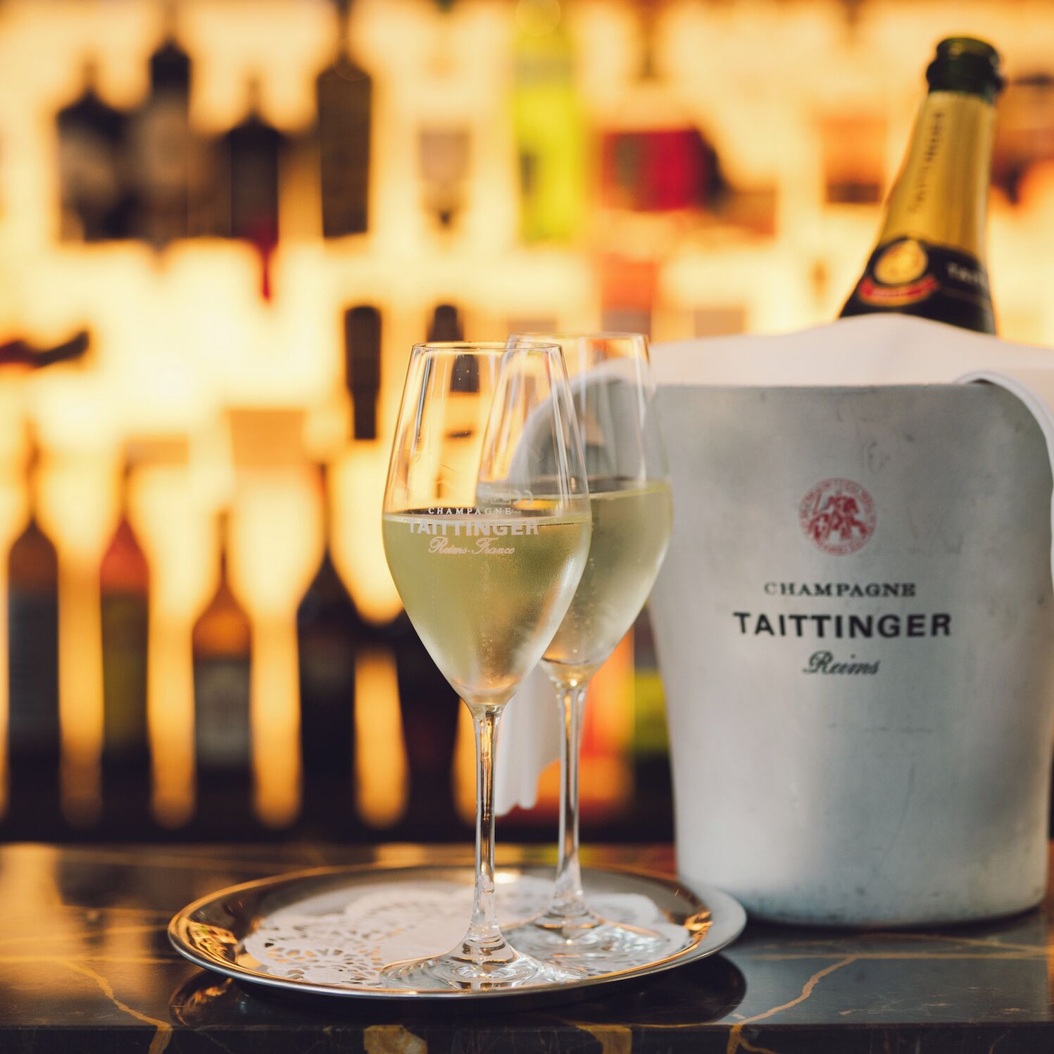 Dos copas de champán sobre una bandeja, con una botella de champán Taittinger al fondo.