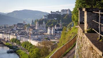 Un paisaje urbano histórico con un castillo imponente en una colina, un río y un paseo de madera a lo largo de un muro de piedra.