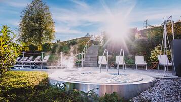 A hot tub surrounded by lounge chairs and a staircase leading to a covered area.