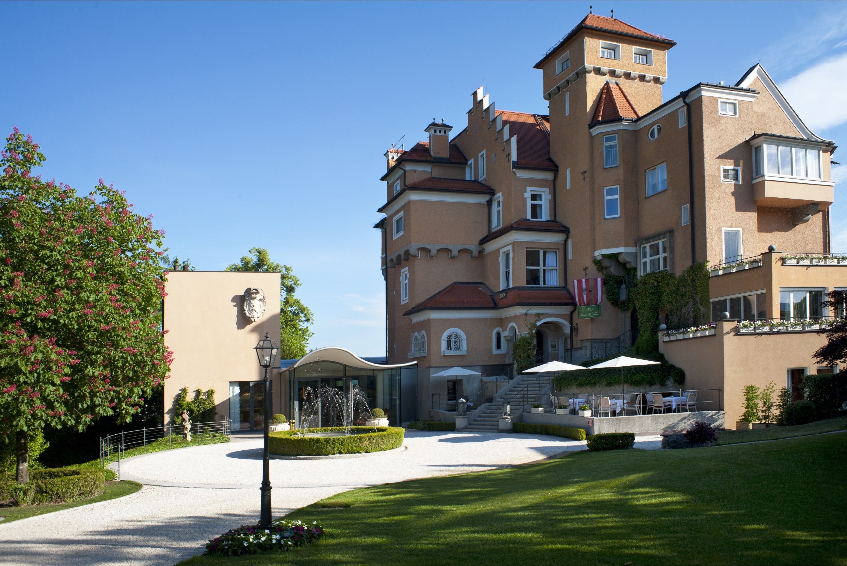 A large, multi-story building with a central courtyard, outdoor seating area, and a fountain.