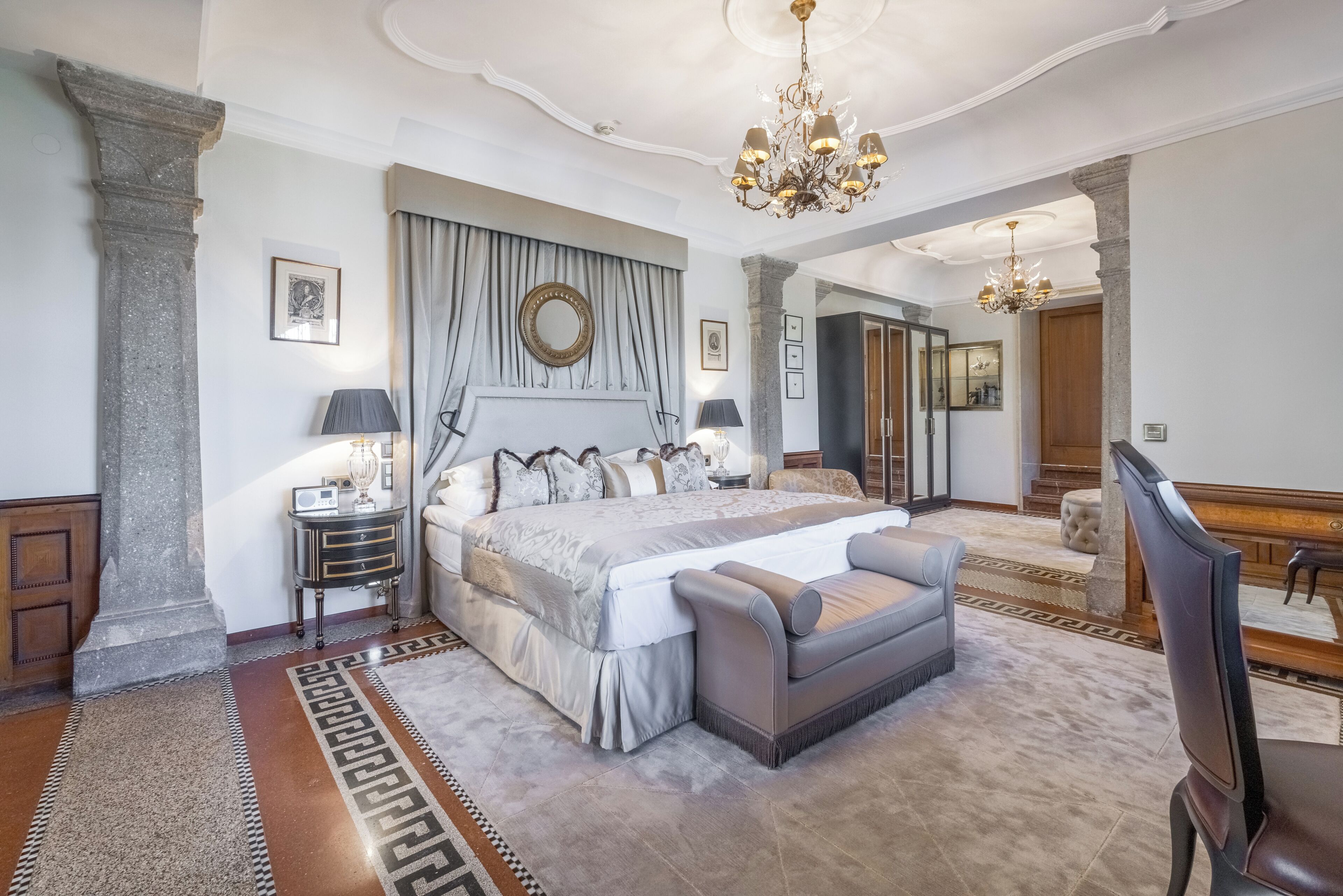Une chambre spacieuse avec un grand lit, un coin salon, un lustre et un miroir.