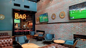 A bar area with leather seating, a television displaying a sports game, and a brick wall.