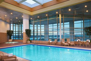 An indoor swimming pool with clear glass walls, lounge chairs, and potted plants. - Courtyard By Marriott Detroit Downtown (Detroit)