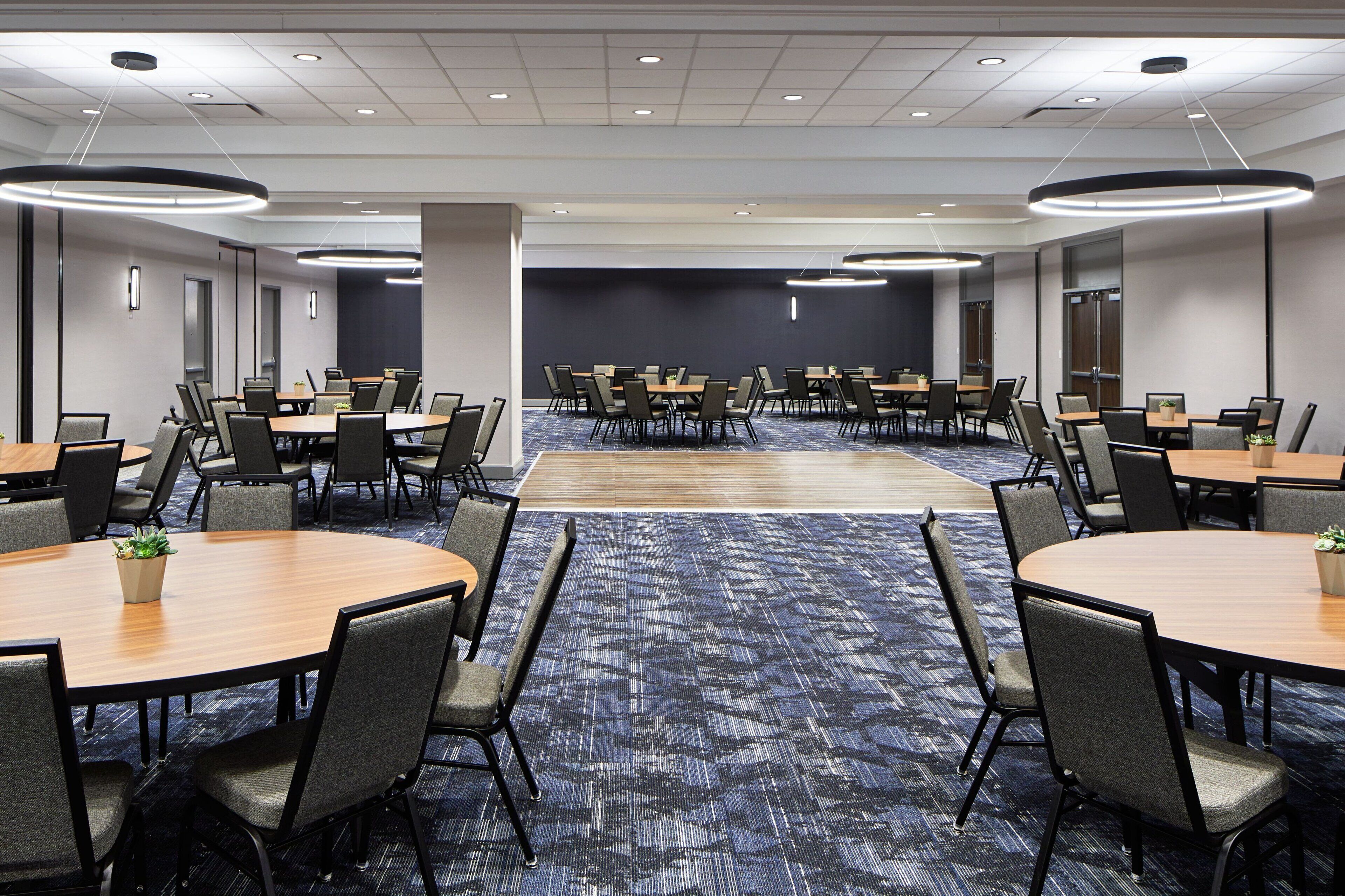 A conference room with multiple tables and chairs, carpeted flooring, and recessed lighting.
