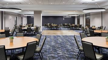 A conference room with multiple tables and chairs, carpeted flooring, and recessed lighting.