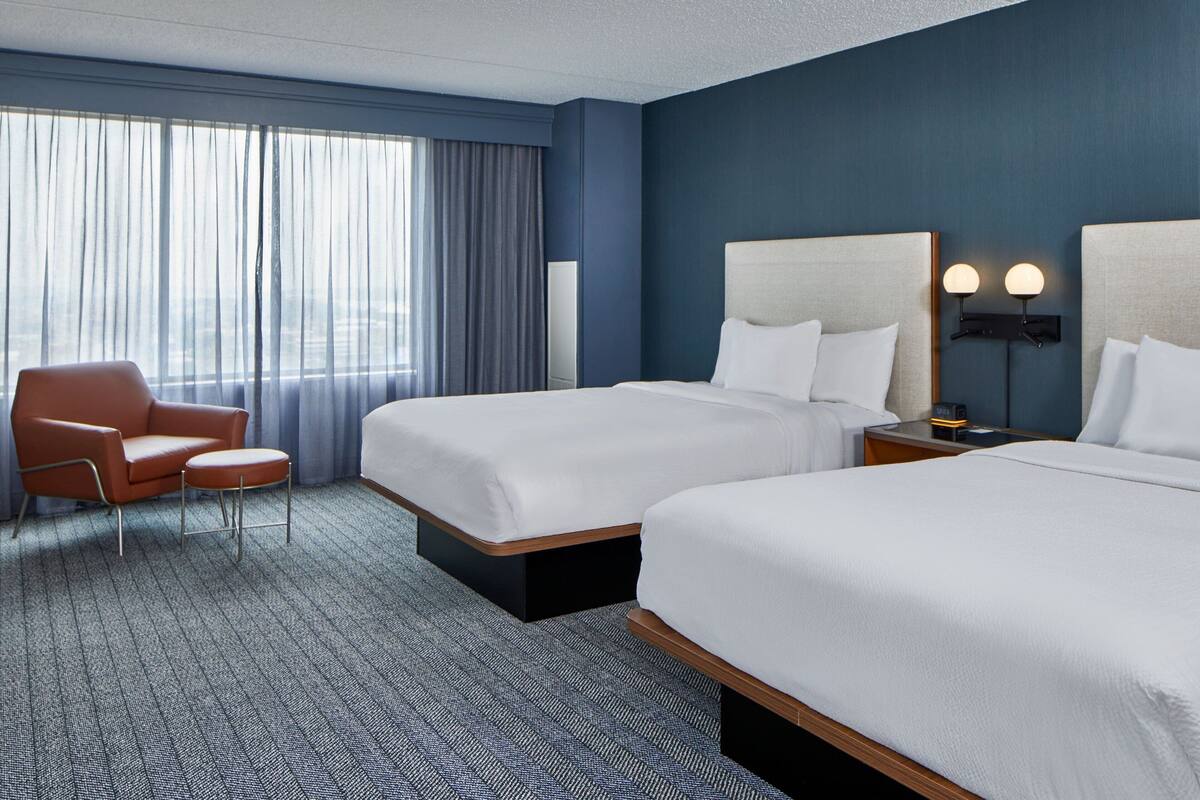 A hotel room with two beds, a sofa, a desk, and a large window with curtains.