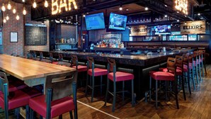 A bar area with a long wooden counter, multiple bar stools, and two televisions mounted on the wall.