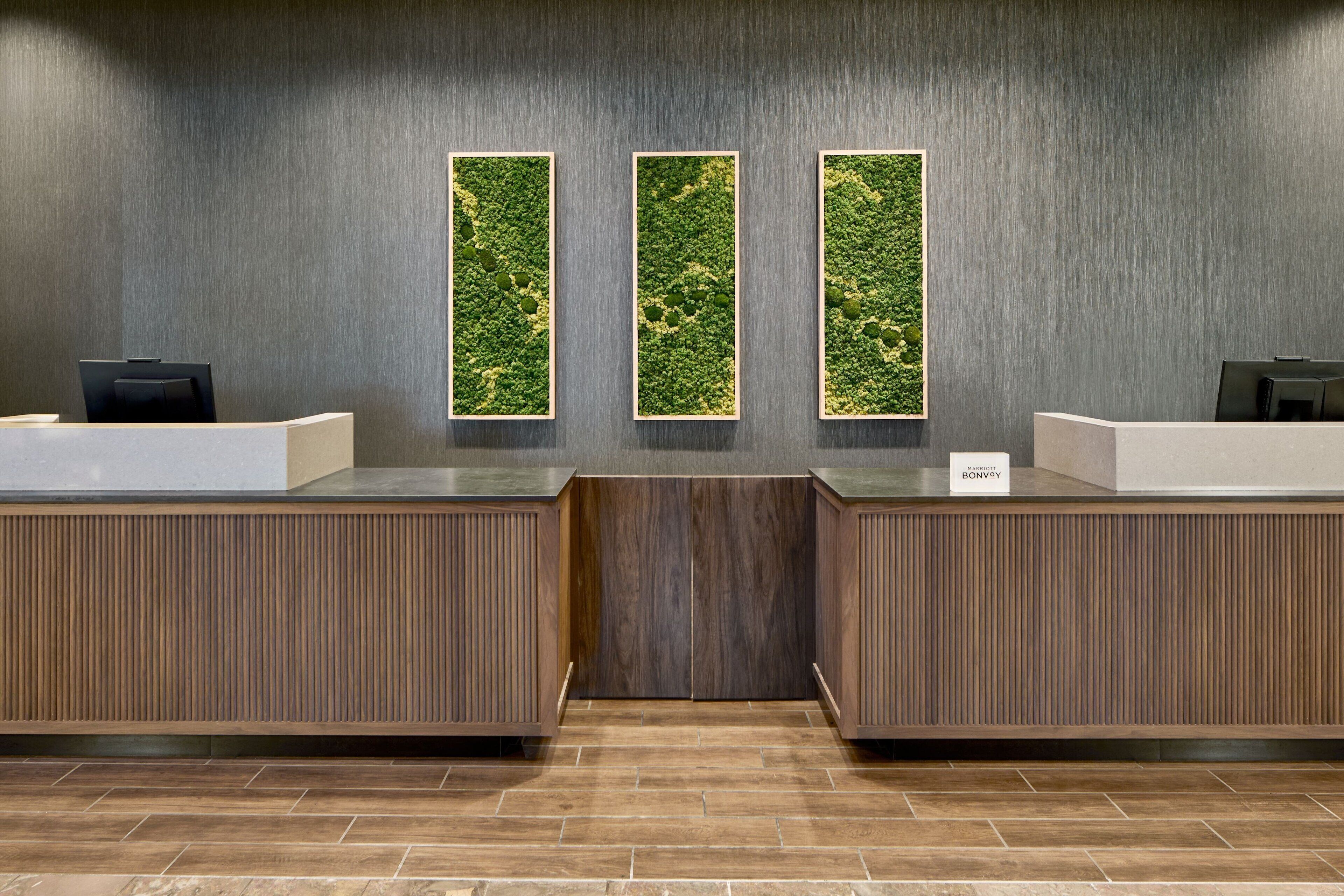 A reception area with a wooden reception desk, a nameplate, and three vertical panels with greenery.