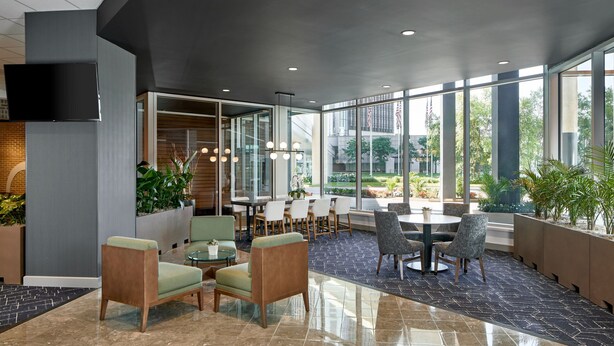 A modern indoor space with seating areas, a dining table, and large windows offering views of the outdoors. - Courtyard By Marriott Detroit Downtown (Detroit)