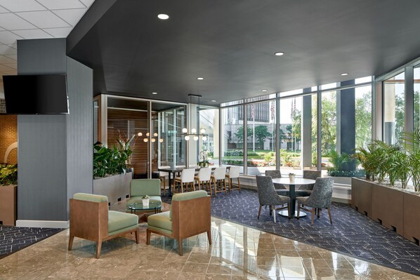A modern indoor space with seating areas, a dining table, and large windows offering views of the outdoors.