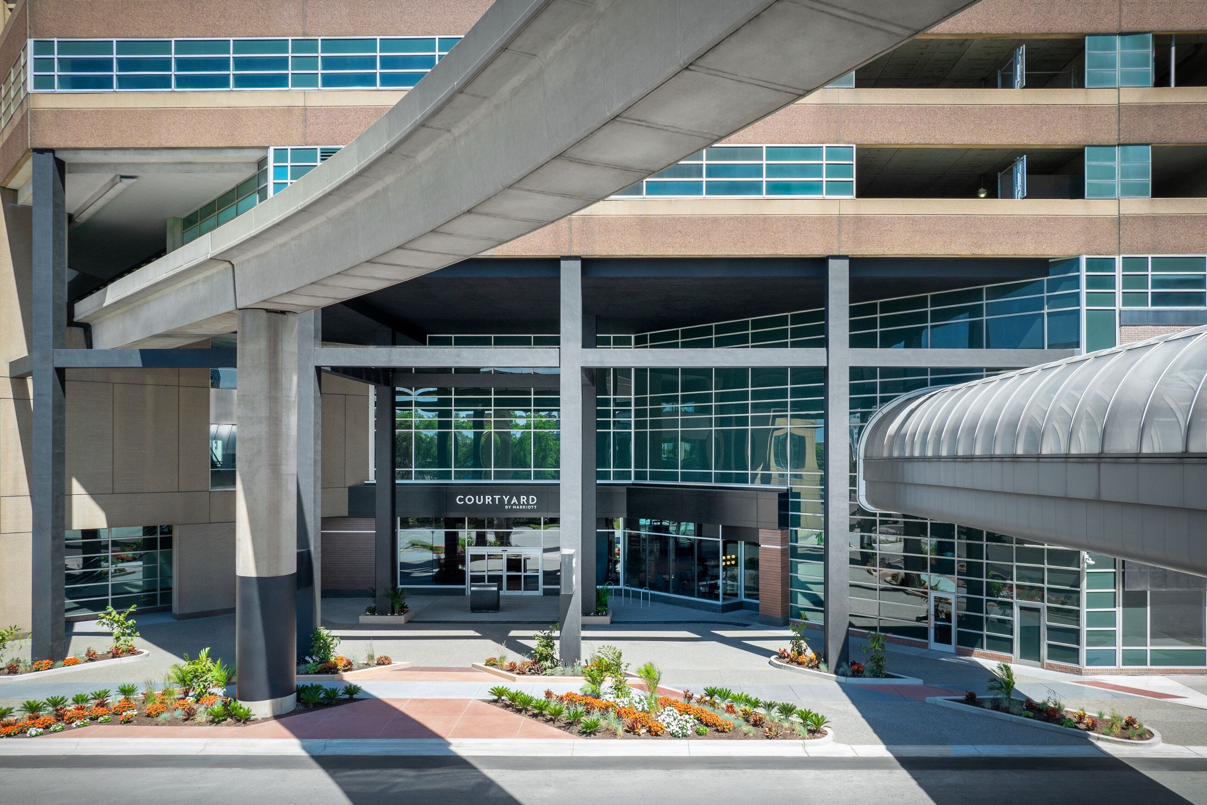 A modern hotel with a glass facade, a covered parking area, and a courtyard with plants.