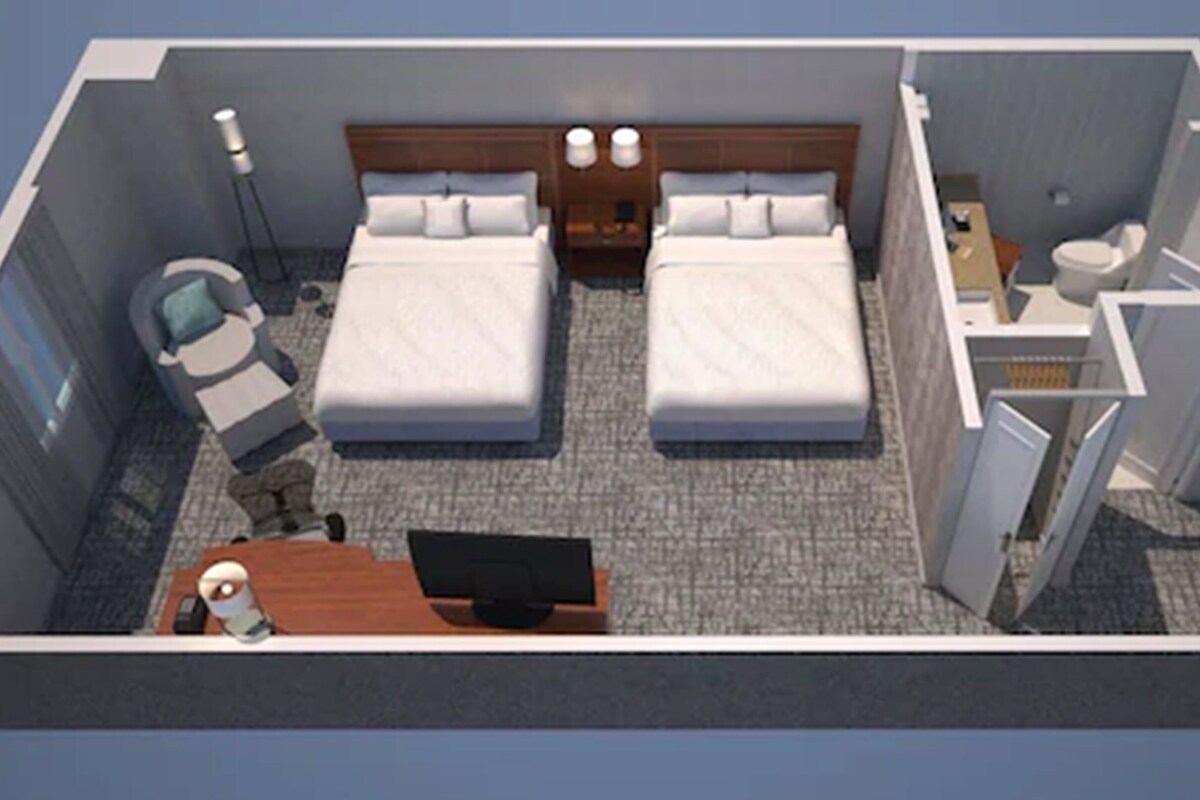 A hotel room with two beds, a desk, a chair, a small table, a lamp, and a window.
