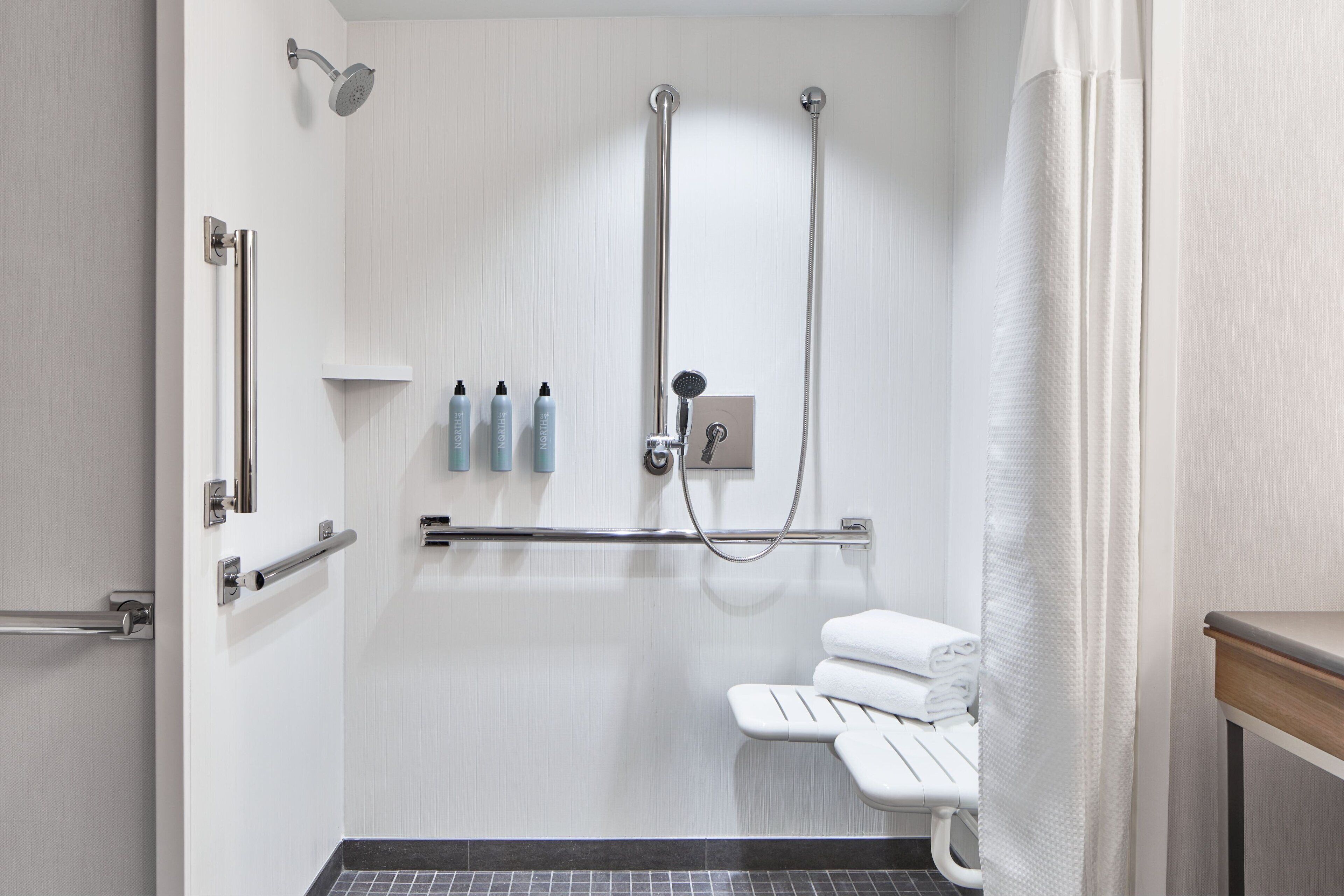 A modern bathroom with a walk-in shower, grab bars, a toilet with a safety seat, and neatly folded towels.