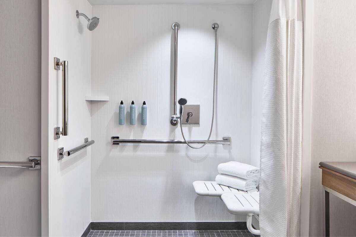 A modern bathroom with a walk-in shower, grab bars, a toilet with a safety seat, and neatly folded towels.