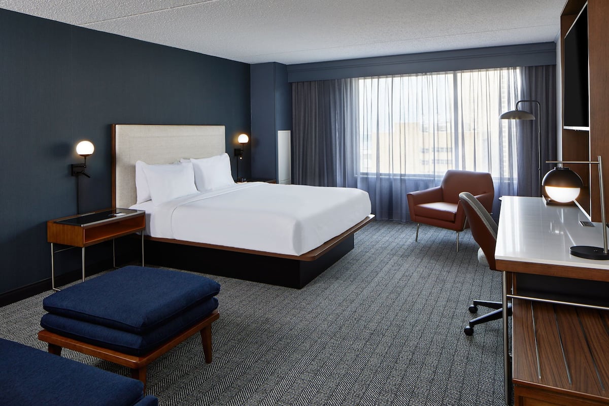 A hotel room with a large bed, a desk, a chair, and a small table.
