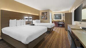 A hotel room with two beds, a desk, a TV, and a bathroom.