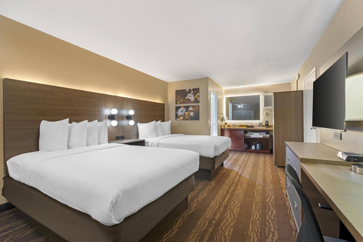 A hotel room with two beds, a desk, a TV, and a bathroom.