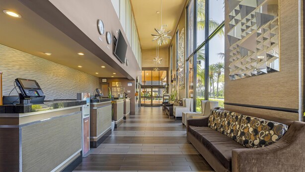 A modern hotel lobby with a reception desk, seating area, and large windows.